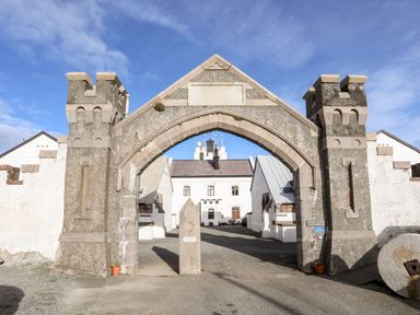 A stone archway entrance to a white building complex with towers and signs at East Point Lynas Lighthouse Keeper's Cottage in Llaneilian near Amlwch