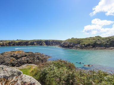 A coastal scene with rocky cliffs and two people kayaking in the water at East Point Lynas Lighthouse Keeper's Cottage Llaneilian near Amlwch
