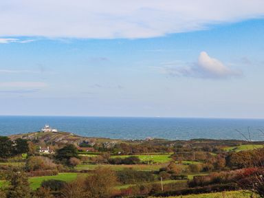 A coastal landscape with green fields houses and a lighthouse on a hill at East Point Lynas Lighthouse Keepers Cottage in Llaneilian near Amlwch