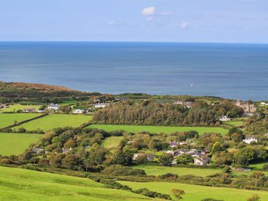 A coastal village with green fields trees and houses by the sea at East Point Lynas Lighthouse Keeper's Cottage Llaneilian near Amlwch