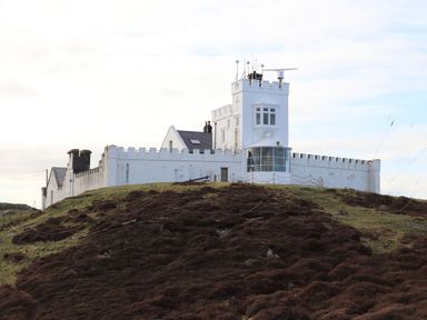 A white lighthouse building on a grassy hill at East Point Lynas Lighthouse Keeper's Cottage in Llaneilian near Amlwch