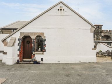 The exterior of a white building with a wooden door, a window, and potted plants near the entrance at West Point Lynas Lighthouse Keeper's Cottage in Llaneilian near Amlwch