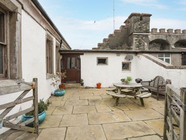 An outdoor patio area with stone flooring wooden picnic table wooden bench potted plants and a wooden gate at West Point Lynas Lighthouse Keeper's Cottage in Llaneilian near Amlwch