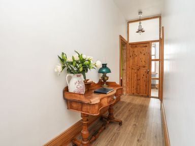 A hallway with a wooden table holding flowers a lamp and a book at West Point Lynas Lighthouse Keeper's Cottage in Llaneilian near Amlwch