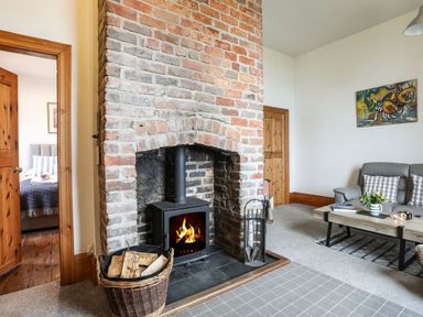 A living room with a brick fireplace a wood stove and a gray sofa with pillows at West Point Lynas Lighthouse Keeper's Cottage Llaneilian near Amlwch