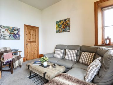 A living room with a leather corner sofa with checkered cushions a wooden door and a wooden coffee table with flowers at West Point Lynas Lighthouse Keeper's Cottage in Llaneilian near Amlwch