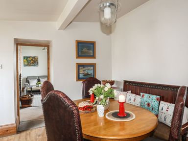 A dining room with a round wooden table and brown chairs next to a bench with cushions at West Point Lynas Lighthouse Keeper's Cottage in Llaneilian near Amlwch