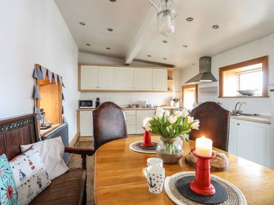 A kitchen with a wooden dining table holding flowers candles and mugs at West Point Lynas Lighthouse Keeper's Cottage Llaneilian near Amlwch