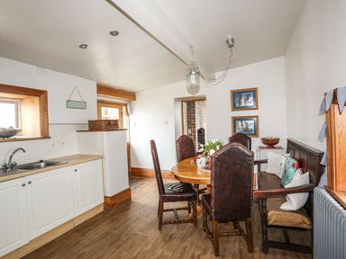 A dining area with leather chairs wooden bench a round table and a kitchen sink area at West Point Lynas Lighthouse Keeper's Cottage in Llaneilian near Amlwch