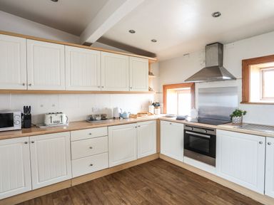 A kitchen with white cabinets wooden countertops a stove microwave toaster kettle and potted plant at West Point Lynas Lighthouse Keeper's Cottage in Llaneilian near Amlwch