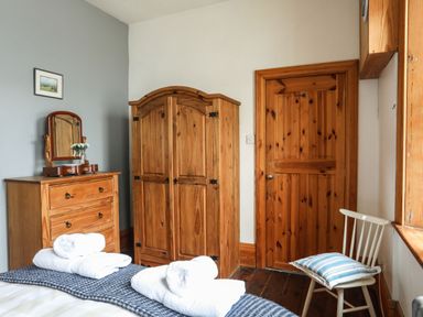 A bedroom with wooden wardrobe and dresser and a chair with cushion at West Point Lynas Lighthouse Keeper's Cottage in Llaneilian near Amlwch