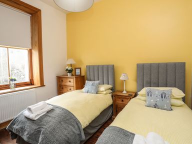 A bedroom with two single beds yellow bedding gray headboards bedside tables window with wooden frame at West Point Lynas Lighthouse Keeper's Cottage in Llaneilian near Amlwch