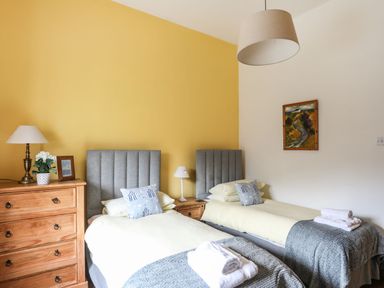 A bedroom with two single beds a wooden chest of drawers and a painting on the wall at West Point Lynas Lighthouse Keeper's Cottage in Llaneilian near Amlwch