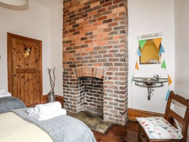 A bedroom corner with a brick fireplace wooden door chair with cushion and a small sink with mirror at West Point Lynas Lighthouse Keeper's Cottage in Llaneilian near Amlwch