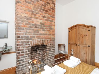 A bedroom with an exposed brick fireplace a wooden wardrobe a wooden chair and a metal bed at West Point Lynas Lighthouse Keeper's Cottage in Llaneilian near Amlwch