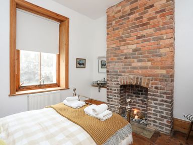 A bedroom with a metal bed frame towels on the bed a window and a brick fireplace at West Point Lynas Lighthouse Keeper's Cottage Llaneilian near Amlwch