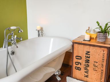 A white freestanding bathtub next to a wooden crate with candles and a plant at West Point Lynas Lighthouse Keeper's Cottage Llaneilian near Amlwch