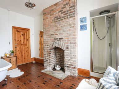 A bathroom with a clawfoot bathtub wooden door brick fireplace and walk in shower at West Point Lynas Lighthouse Keeper's Cottage Llaneilian near Amlwch
