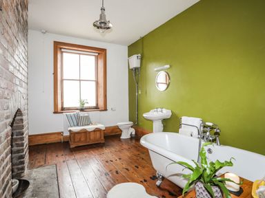 A bathroom with a bathtub, sink, toilet, window seat, and a brick fireplace at West Point Lynas Lighthouse Keeper's Cottage in Llaneilian near Amlwch