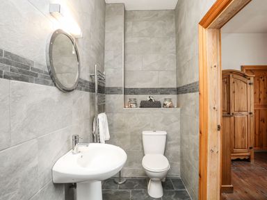 A bathroom with a toilet sink round mirror and towel rack at West Point Lynas Lighthouse Keeper's Cottage in Llaneilian near Amlwch
