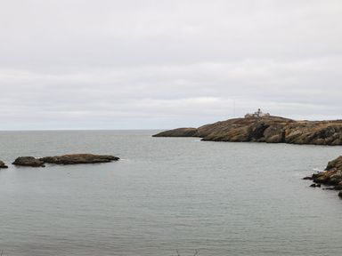 A coastal scene with rocky land and buildings on a hill near the water at West Point Lynas Lighthouse Keeper's Cottage in Llaneilian near Amlwch