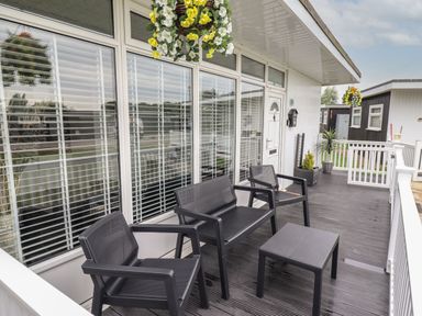 An outdoor patio with black chairs a table hanging flower baskets and potted plants at 39 Cherry Park in Chapel St Leonards