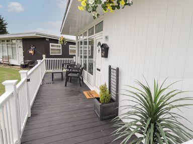A porch with chairs a table and plants at 39 Cherry Park in Chapel St Leonards