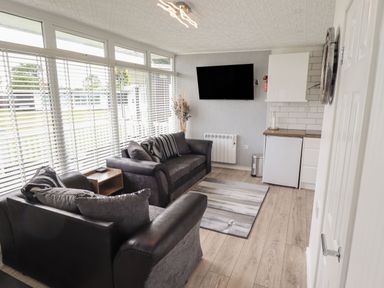 A living room with two sofas a wall-mounted TV and a small kitchen area at 39 Cherry Park in Chapel St Leonards