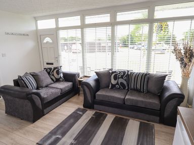 A living room with two sofas a striped rug and a vase with dried plants at 39 Cherry Park in Chapel St Leonards
