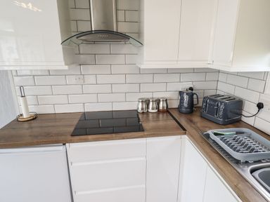 A kitchen with white cabinets wooden countertops induction stove kettle toaster and dish rack at 39 Cherry Park in Chapel St Leonards