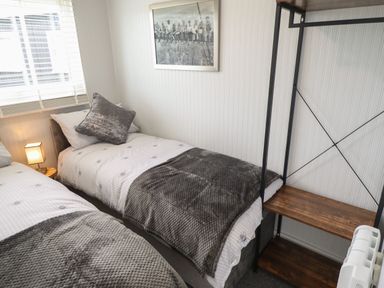 A bedroom with two single beds a wooden shelf unit a lamp on a side table and a framed picture on the wall at 39 Cherry Park in Chapel St Leonards