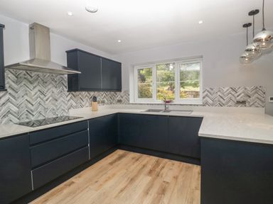 A kitchen with dark cabinets white countertops a window and wood flooring at Ranbir House in Longhope