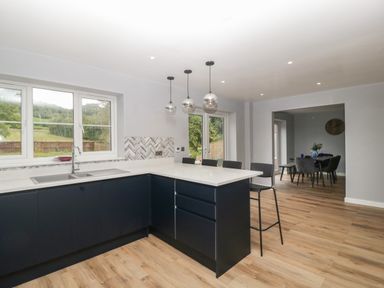 A kitchen with dark cabinets a white countertop a sink a window and pendant lights next to a dining area at Ranbir House in Longhope