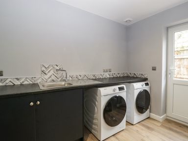 A laundry room with a washing machine dryer black countertop sink and door at Ranbir House in Longhope