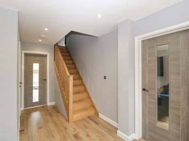 A hallway with wooden stairs and two wooden doors with glass panels at Ranbir House in Longhope