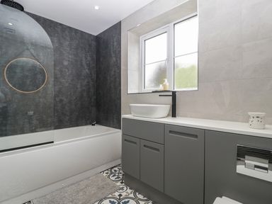 A bathroom with a bathtub a gray cabinet with a sink and a window at Ranbir House in Longhope