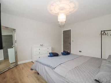 A bedroom with a bed covered in gray bedding two sets of folded towels on top a white dresser with a small flower arrangement a large floor mirror and a hanging clothing rack at Ranbir House in Longhope