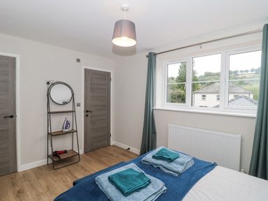 A bedroom with bed towels on it a window with curtains a radiator two doors and a shelving unit with a mirror an iron and hair dryer at Ranbir House in Longhope