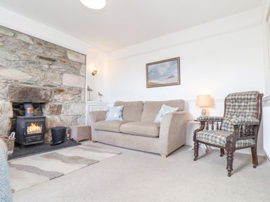 A living room with a stone fireplace a beige sofa a plaid armchair and a framed painting at Crab Pot Cottage in Porthleven