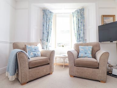 A sitting area with two armchairs and a small round table in front of a window at Crab Pot Cottage in Porthleven