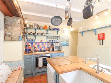 A kitchen with hanging pans blue shelves pots and pans a stove sink and wooden countertops at Crab Pot Cottage in Porthleven
