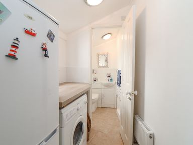 A utility room with a washing machine refrigerator and a view into a small bathroom at Crab Pot Cottage Porthleven