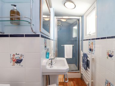 A bathroom with a sink shower and decorated wall tiles at Crab Pot Cottage in Porthleven