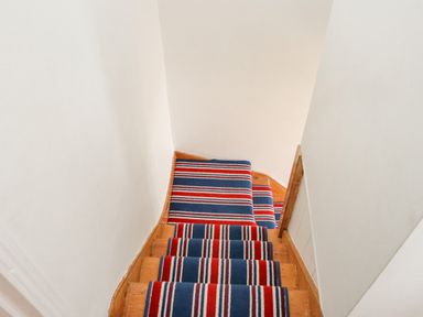 A staircase with wooden steps covered by a blue and red striped carpet at Crab Pot Cottage in Porthleven
