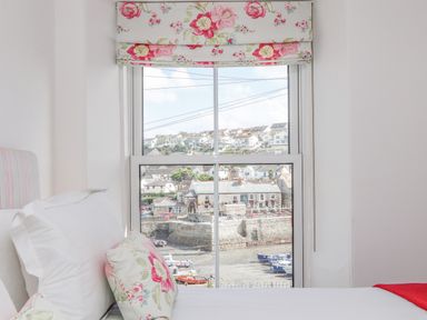 A bedroom window with floral curtains looking out to boats and houses at Crab Pot Cottage in Porthleven