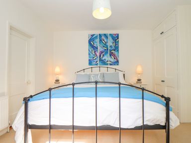 A bedroom with a black metal bed frame blue blanket and artwork above the bed at Crab Pot Cottage in Porthleven