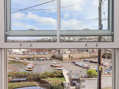 A view of a harbor with boats and houses through a window at Crab Pot Cottage in Porthleven