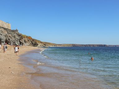A sandy beach with people walking and swimming next to rocky cliffs at Crab Pot Cottage in Porthleven