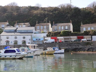 Boats moored in water near a stone wall with buildings and houses behind a wooded hillside at Crab Pot Cottage in Porthleven