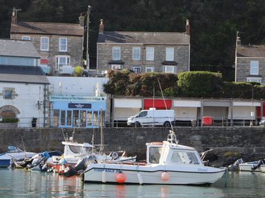Boats docked in a harbor with stone houses and a restaurant in the background at Crab Pot Cottage in Porthleven